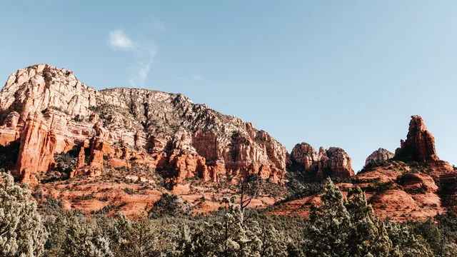 Red rock cliffs and pine trees under a blue sky in Arizona.