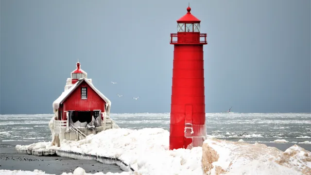 A red lighthouse and a small red pier house in snow and ice on Lake Michigan.