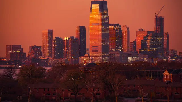 Skyscrapers glowing orange at dusk across the water in New Jersey.