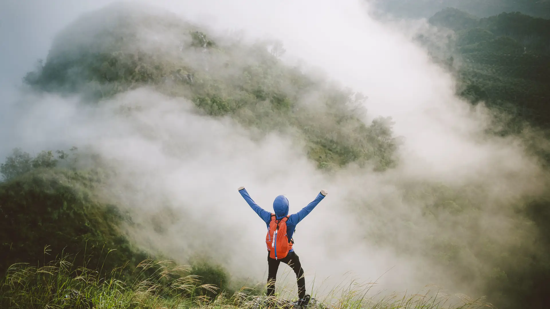 A traveler with arms raised on a mountain top, looking out over the clouds