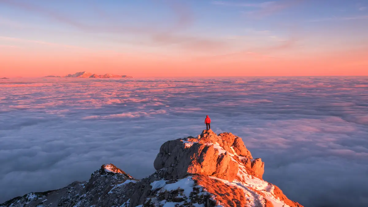 A traveler on a mountain peak above low clouds